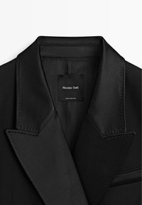 Schwarzer Blazer mit satinierter Oberfläche, aufgeschlagenen Revers und einer Tasche. Das Innenetikett trägt die Aufschrift "Massimo Dutti" und "Made in Portugal".