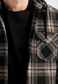 Skotskrandet flannel skjorte i sort og beige, med en hætte, knapper og en brystlomme. Sammen med en sort crewneck t-shirt under.
