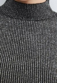 Schwarzes geripptes Rollkragenoberteil mit metallic-silbernem Faden. Der Stoff hat eine weiche Textur, eine figurbetonte Silhouette und einen hohen Kragen.