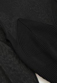 Prim-plan al unui material textil negru, evidențiind modele de tricotaj distincte cu secțiuni ribbate și texturi transparente.