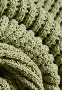 Gros plan d'un tissu tricoté épais vert clair montrant de grosses mailles texturées et des plis ondulés.