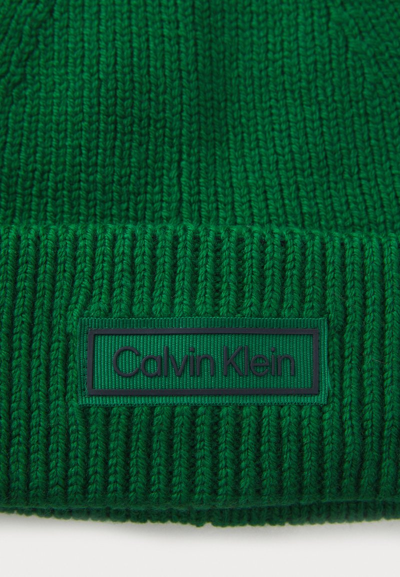 Groene gebreide beanie met een geribbelde textuur en een plat, rechthoekig Calvin Klein logo label in donkergroen op de boord.