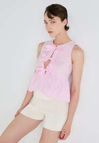 Roze en witte gestreepte mouwloze top met drie strikken en een peplum ontwerp, gecombineerd met witte gebreide shorts die een gestructureerde afwerking hebben.