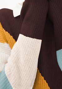 Pull en tricot avec un design coloré, présentant des sections marron, jaune moutarde, crème et bleu clair. Tissu texturé avec des motifs contrastants.