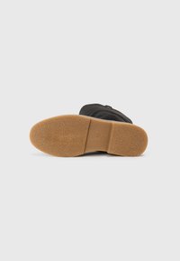 Chaussures noires avec une tige texturée, semelle extérieure en caoutchouc et semelle beige. Présente une finition lisse et un design à bout arrondi.