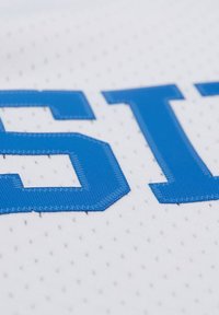 Weißes Netzgewebe mit kräftig blauen gestickten Buchstaben "EST" und strukturiertem Finish. Der Hintergrund zeigt ein perforiertes Muster.