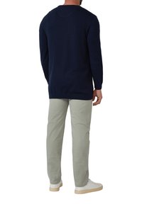 Marineblauwe trui met een ronde hals, lange mouwen en geribbelde boorden, gecombineerd met lichtgroene broek en witte sneakers. Eenvoudig, casual ontwerp.