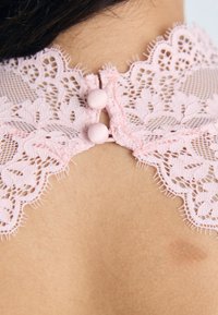 Ροζ κεντητός γιακάς με λουλουδάτα σχέδια και οδοντωτή άκρη, καθώς και δύο κουμπιά καλυμμένα με ύφασμα στο πίσω μέρος, σε φόντο με τόνο δέρματος.