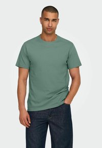 Green cotton t-shirt with a round neck and short sleeves, paired with dark blue denim jeans. Plain design, no visible patterns or logos.