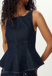 Tmavý denimový top s peplum střihem, výstřihem ve tvaru lodičky, kontrastním prošíváním a přiléhavým tělem, které se na pase rozšiřuje. Bez viditelných zapínání.