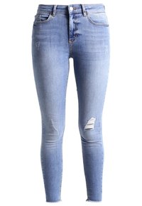 Jeans de corte ajustado en denim azul claro. Presentan detalles desgastados y bajos deshilachados. Diseño clásico de cinco bolsillos con cierre de botón.