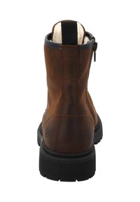 Brązowy skórzany botek za kostkę z czarną pętelką, czarną gumową podeszwą, zamkiem błyskawicznym z boku oraz widoczną białą owczą wełną na górze.