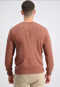 Felpa di cotone marrone con polsini e orlo a costine, caratterizzata da una patch rettangolare sul retro. Texture liscia, vestibilità rilassata.