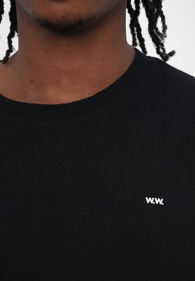 Tricou negru din bumbac, cu guler rotund, având un logo alb "W.W." pe partea stângă a pieptului. Textură fină, guler cu nervuri.