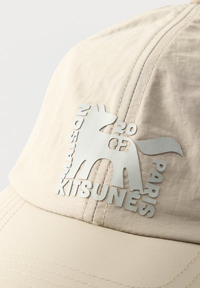 Μπεζ καπέλο με ανάγλυφο λογότυπο ασημί αλεπούς και κείμενο που γράφει "MAISON KITSUNÉ," "PARIS," και "2020 03" στο μπροστινό πάνελ.