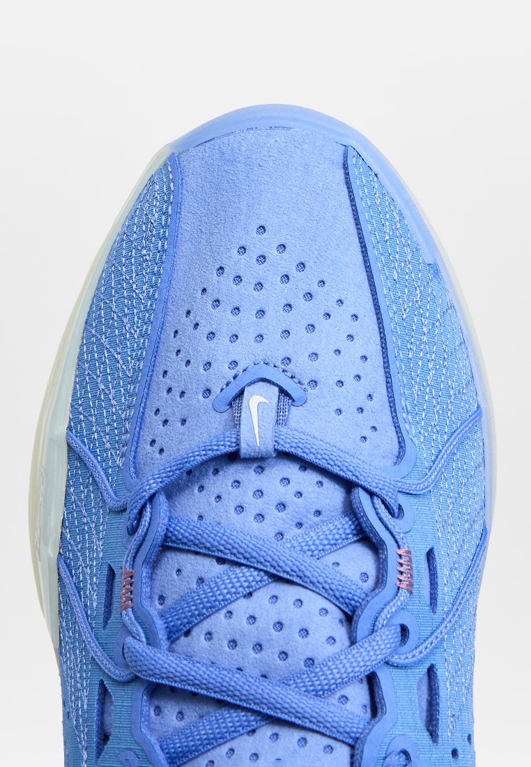 Zapatilla deportiva azul con una parte superior texturizada, perforaciones para transpirabilidad y una suela translúcida. Presenta un logotipo prominente y cordones.