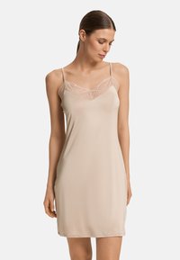 Vestido de tirantes nude de tejido suave, con detalles de encaje en el escote y tirantes finos ajustables. Diseño de longitud media con una textura suave.