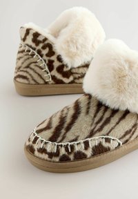 Slapi pufoși cu model bej și maro, cu margine din blană sintetică, având cusături albe și talpă din cauciuc. Textură moale, design low-top.