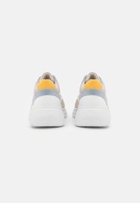 Baskets avec une semelle blanche et différentes textures supérieures en gris doux, jaune et beige. Les détails comprennent un embout lisse et un col rembourré.