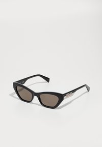 Ochelari de soare negri în formă de ochi de pisică, cu lentile maro, având o finisare lucioasă și un accent metalic cu logo pe brațe. Design unghiular, îndrăzneț.