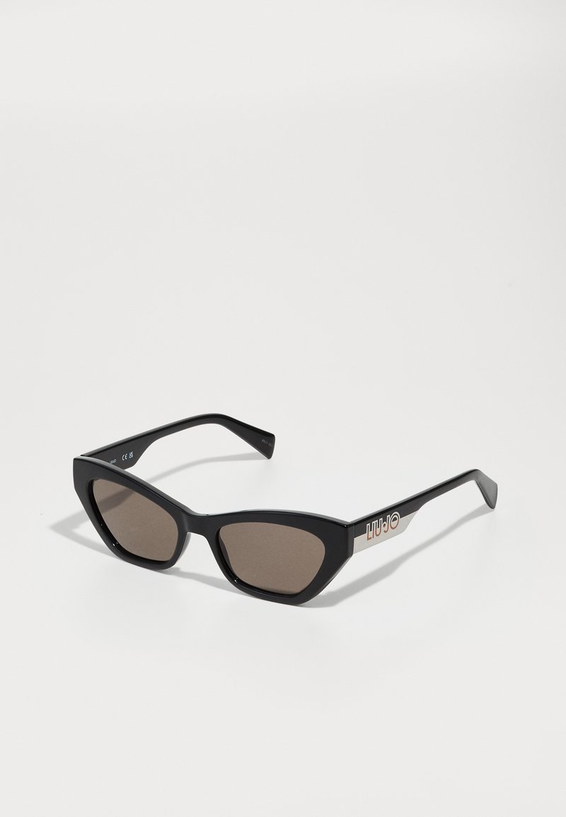 Ochelari de soare negri în formă de ochi de pisică, cu lentile maro, având o finisare lucioasă și un accent metalic cu logo pe brațe. Design unghiular, îndrăzneț.