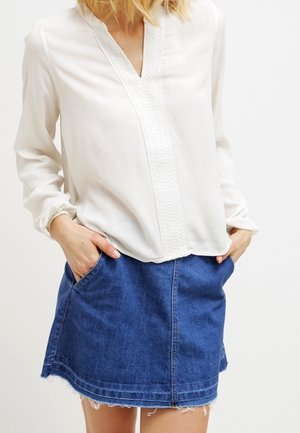 Biała, długorękawowa bluzka z dekoltem w serek i fakturowanym przodem, zestawiona z niebieską spódnicą denimową z przednimi kieszeniami i postrzępionym dołem.
