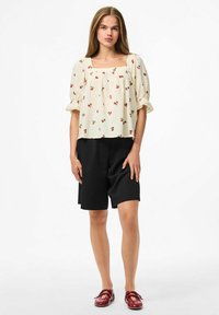 Camicia bianca con piccola stampa di ciliegie rosse, scollatura quadrata, maniche a sbuffo, abbinata a pantaloni corti neri e scarpe rosse. Tessuto dalla texture liscia.