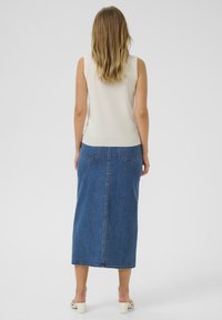 Haut sans manches crème avec une texture côtelée, associé à une longue jupe en denim bleu à coupe droite et poches arrière.