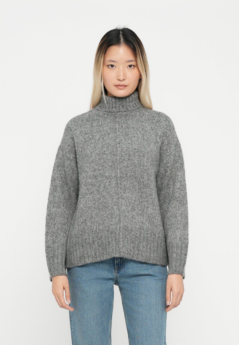 Hallgray turtleneck-sviiter ribaste tekstuuriga, millel on langenud õlad ja mugav lõige, koos helesiniste teksadega.