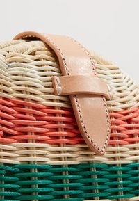 Panier tissé avec des bandes naturelles, orange et vertes, fixé par une sangle en cuir beige clair avec détails de couture.