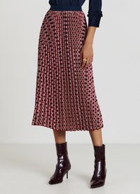 Jupe plissée à motif rouge et crème avec une taille cintrée et un ourlet à hauteur du genou, associée à des bottines brillantes foncées.