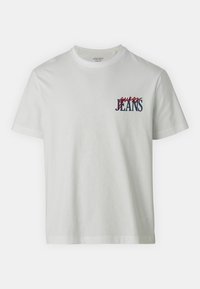 Balta medvilninė marškinė su apvalia iškirpte ir trumpomis rankovėmis, priekyje kairėje pusėje yra raudonas ir mėlynas "guess JEANS" grafikas.