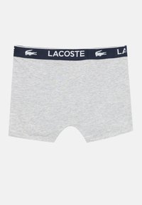 Boxer corti grigi realizzati in un morbido tessuto testurizzato. Presentano un elastico in vita blu navy con il marchio e il logo "LACOSTE" in bianco.