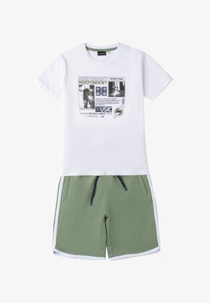 Witte katoenen t-shirt met grafische print en tekst, gecombineerd met groene shorts met een trekkoord en witte zijstrepen.