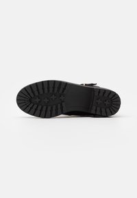 Suela de zapato negra con diseño de goma texturizada, que presenta un patrón de agarre ancho y un diseño plano para una mayor tracción. Los acentos del empeine son visibles en los lados.