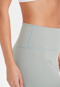 Höga leggings i ljusgrått, tillverkade av mjukt elastiskt material. Har kontrasterande ljusblå sömmar längs kanterna.