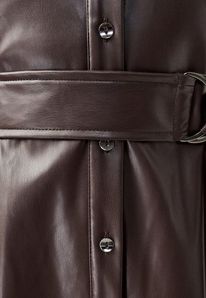 Bruine leren bovenkleding heeft een gladde textuur, een ceintuur in de taille en zilveren knoopaccenten, wat een gestructureerd ontwerp en een gepolijste afwerking benadrukt.