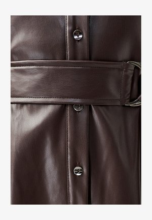 Bruine leren bovenkleding heeft een gladde textuur, een ceintuur in de taille en zilveren knoopaccenten, wat een gestructureerd ontwerp en een gepolijste afwerking benadrukt.