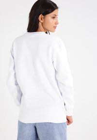 Sudadera blanca hecha de un tejido suave, con un escote redondo y puños acanalados. La vista trasera muestra un diseño simple y limpio, sin adornos.