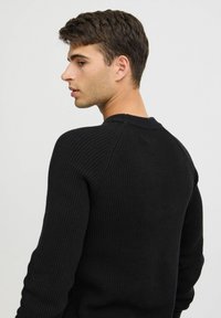 Pulover negru din tricot rib sapat, cu mâneci lungi, guler rotund și cusături raglan, evidențiind un material texturat și un design ajustat.