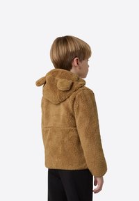 Rjava flis jakna s kapuco, ki ima poudarke v obliki ušes, teksturirano tkanino in sproščen kroj, videna od zadaj.