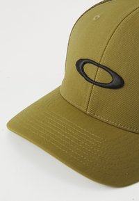 Olivengrønn baseballcaps med buet skygge og svart ovallogo brodert på frontpanelet, satt mot en hvit bakgrunn.