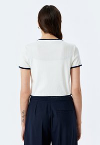 Korte mouwen, witte top met een geribbelde textuur en marineblauwe accenten op de kraag en mouwen, gecombineerd met marineblauwe hoog-gewijze broek.