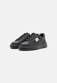 Zapatillas de cuero negro con un acabado suave, punta redondeada, suela plana, cordones contrastantes y un pequeño logotipo metálico en un lateral.