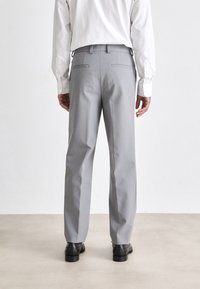 Pantalones grises a medida con un corte relajado, que presentan una textura suave, bolsillos laterales y traseros, combinados con zapatos negros.