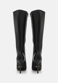 Crne kožne čizme do koljena s modernim dizajnom, uskim vrhovima i štiklama na stiletto. Imaju patentne zatvarače na stražnjoj strani i diskretni logo brenda na peti.