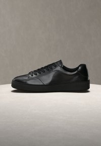 Μαύρο sneaker χαμηλό δερμάτινο με κορδόνια μπροστά και παχιά σόλα από καουτσούκ σε φωτεινή επιφάνεια με ουδέτερο φόντο.