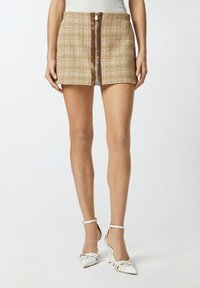 Smešani smeđi karirani mini suknja s prednim zatvaračem, uparena s bijelim sandalama na visoku petu s vertikalnim prugama i šiljatim vrhovima.