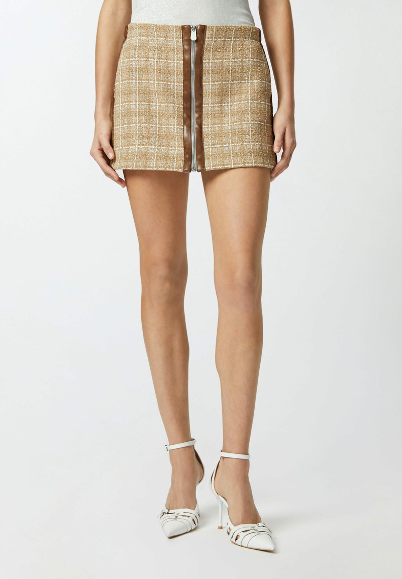 Smešani smeđi karirani mini suknja s prednim zatvaračem, uparena s bijelim sandalama na visoku petu s vertikalnim prugama i šiljatim vrhovima.