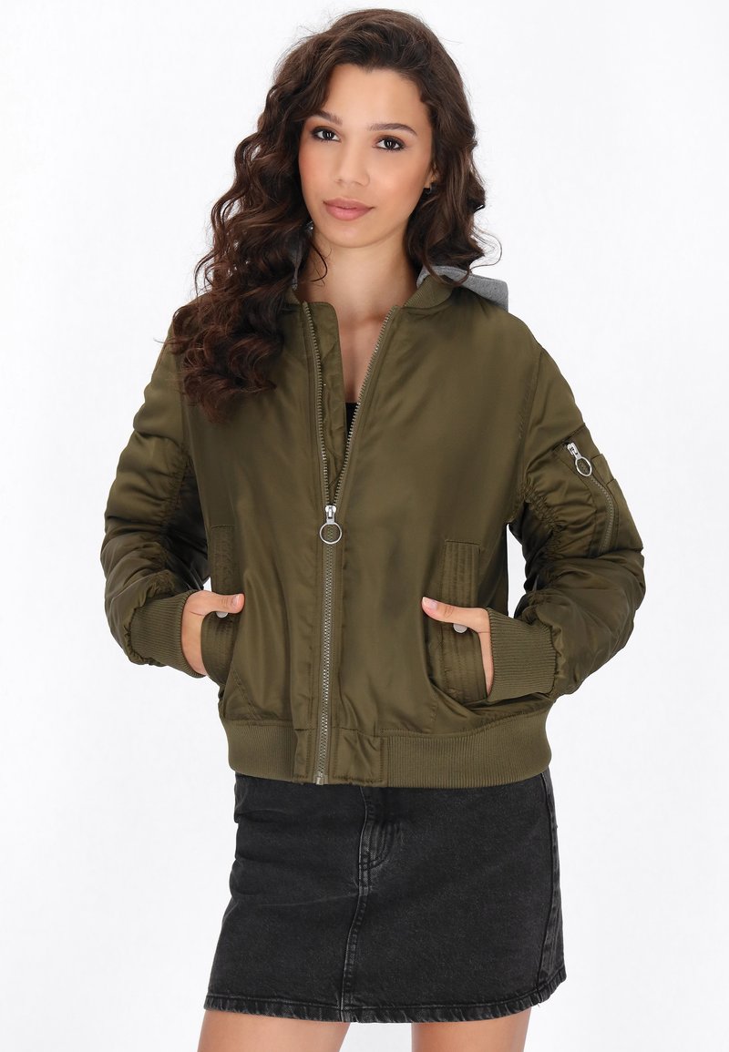 Giacca bomber verde oliva con zip frontale, polsini a costine e due tasche frontali. Presenta un cappuccio grigio e un tessuto strutturato.